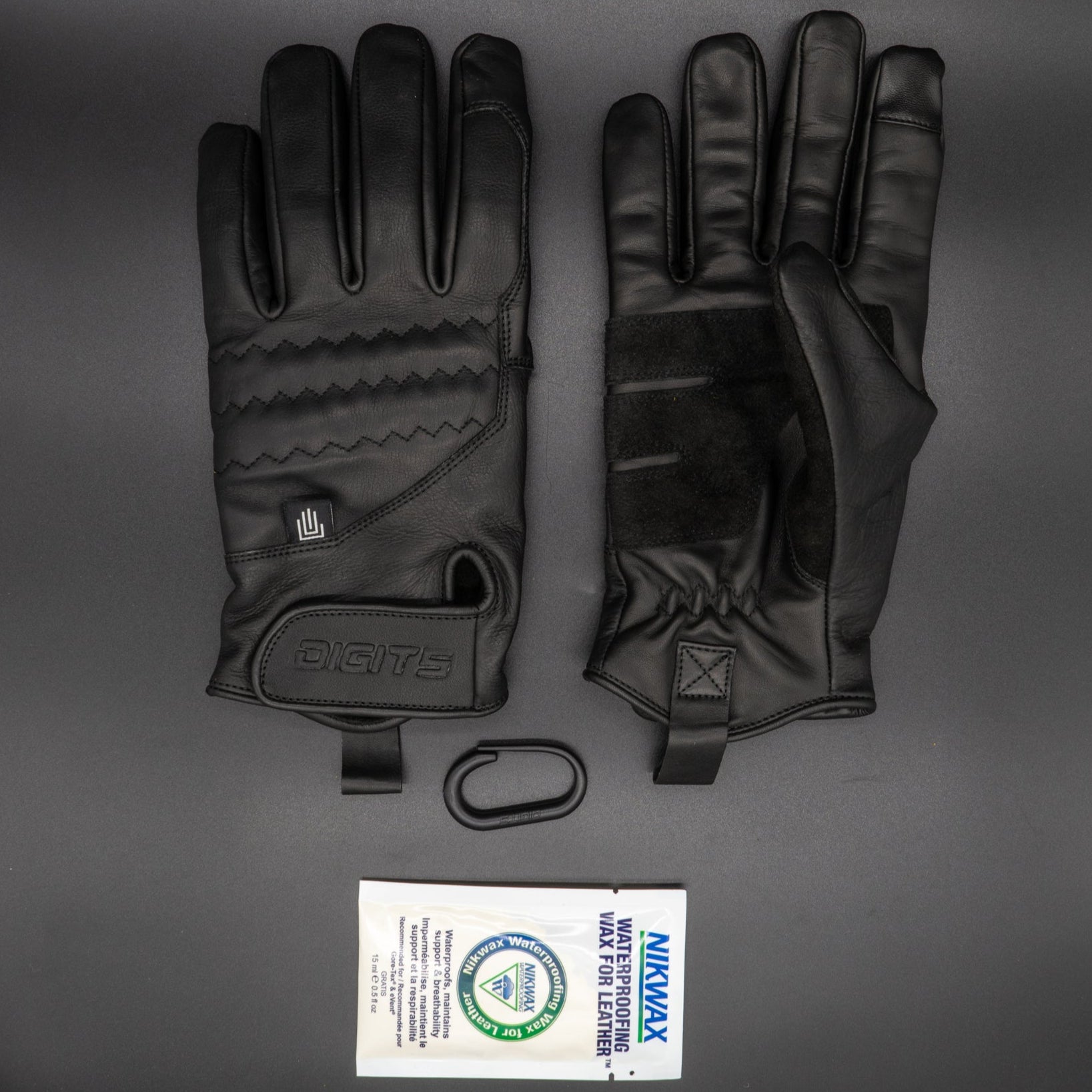 A pair of black, insulated leather work gloves with extended cuffs and Velcro wrist closures, displayed palm-up with a company logo on the Velcro strap, alongside a package of Nikwax leather waterproofing.